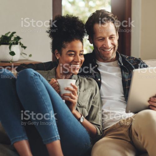 Shot of a happy young couple using a digital tablet together while relaxing on a couch at home